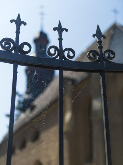 A wrought-iron fence with intricate spikes. In the background, a blurry church building can be seen.