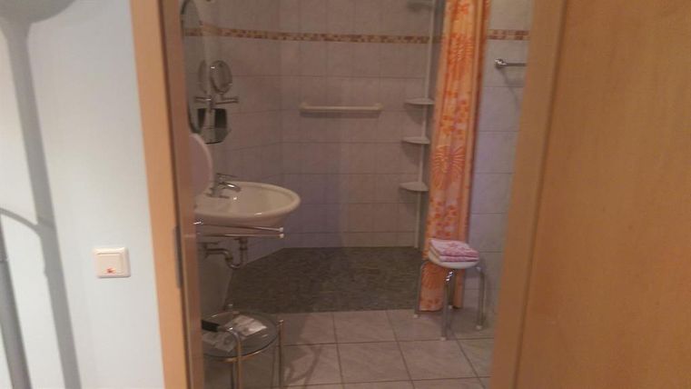 A simple bathroom with a shower and a sink. The walls are tiled and there is a shower curtain in warm colors.