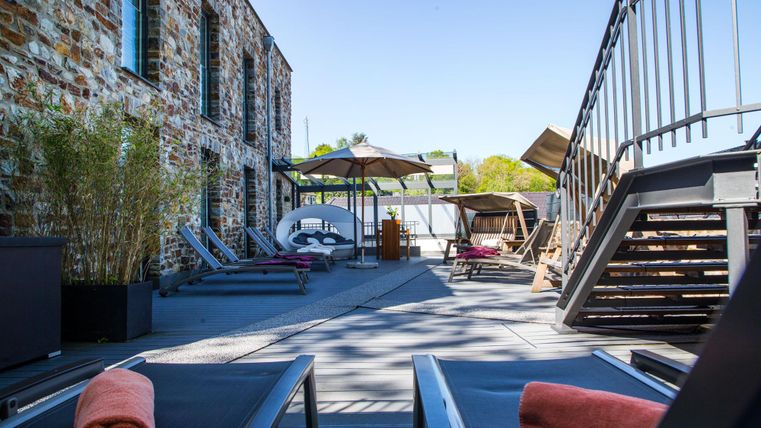 A modern terrace with loungers and sun umbrellas. In the background, stone walls and a beautiful landscape can be seen.