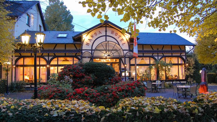Ein charmantes Restaurant mit großen Fenstern und einem einladenden Eingang. Umgeben von buntem Laub und schönen Blumen im Garten.