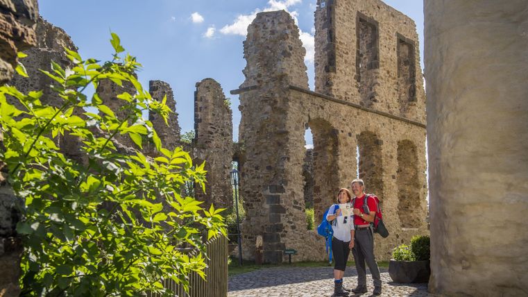 Eine beeindruckende Ruine mit großen Steinen und einem blauen Himmel. Zwei Personen stehen davor und genießen die Aussicht.