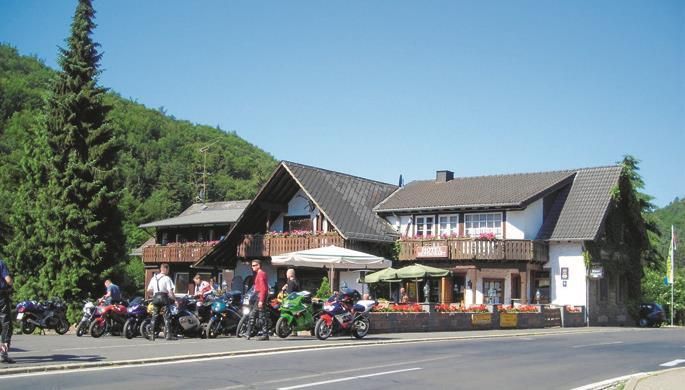 A cozy inn with a large balcony in a green environment. Several motorcycles are parked in front of the house.