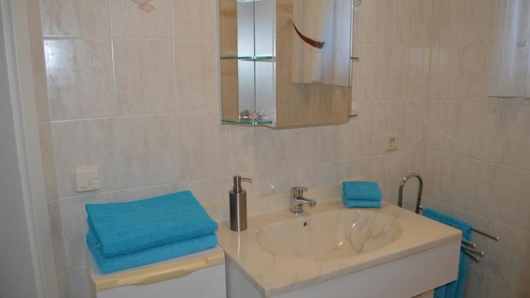 Ein modernes Badezimmer mit einem Waschbecken und einem großen Spiegel. Die Handtücher und Accessoires in Türkis verleihen dem Raum einen frischen Look.