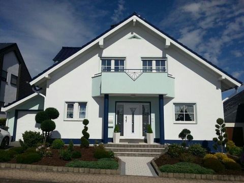 Ein modernes, weißes Haus mit blauen Akzenten. Der gepflegte Vorgarten hat mehrere Bäume und Sträucher.