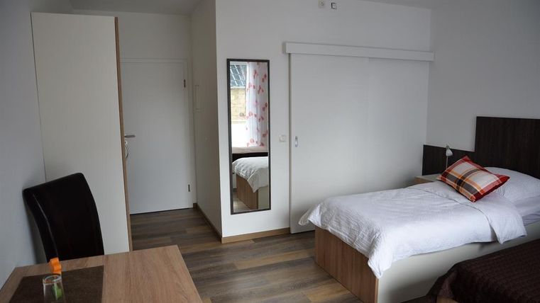 Ein einfaches Schlafzimmer mit einem Einzelbett und einem kleinen Tisch. Der Raum hat einen modernen Look und Holzboden.