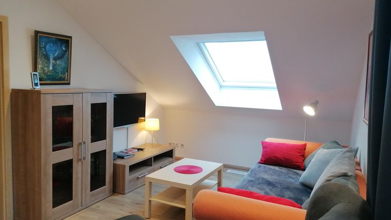 A cozy living space with a gray and an orange sofa. The room features a television, a table, and a skylight that provides natural light.