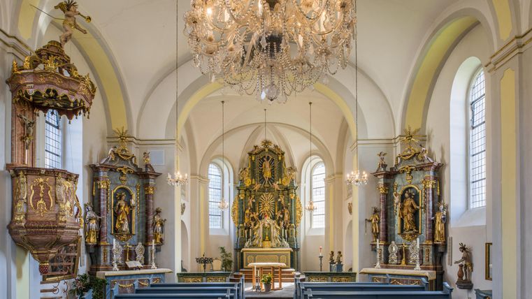 Eine wunderschöne Kirche mit hohen Decken und einem großen Kronleuchter. Der Altarbereich ist detailliert mit religiösen Figuren geschmückt.