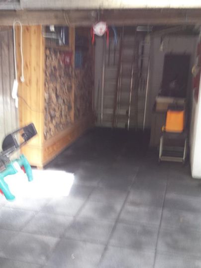 Eine garage mit schwarzen Fliesen und Holzlagerung an der Wand. Im Hintergrund sind eine Leiter und ein Stuhl zu sehen.