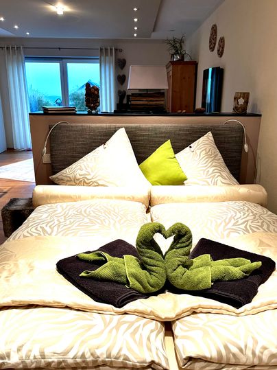 Ein gemütliches Schlafzimmer mit einem Doppelbett und dekorativen Kissen. Im Bett liegen kunstvoll gefaltete Handtücher in Form von Schwänen.
