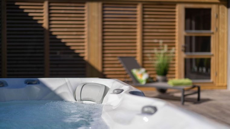 Ein entspannender Whirlpool auf einer sonnigen Terrasse. Im Hintergrund sind moderne Holzelemente und Pflanzen zu sehen.