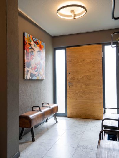 Ein moderner Flur mit einem großen Holzauftür und einem bunten Gemälde an der Wand. Die Einrichtung ist schlicht und zeitgemäß, mit Sitzgelegenheiten aus Holz.