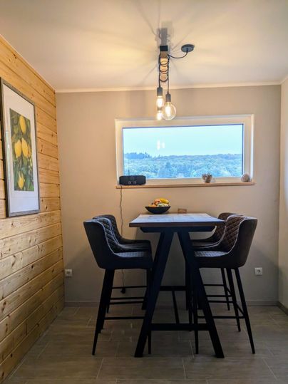 Ein moderner Essbereich mit einem Tisch und Stühlen. Große Fenster bieten einen Blick auf die Landschaft.