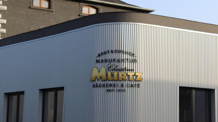 Ein modernes Gebäude mit einer eleganten Fassade. Die Fassade trägt das Schild einer Bäckerei und Café namens "Murtz".