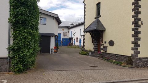 Eine ruhige Straße mit zwei Häusern und einem gepflasterten Weg. Die Häuser haben verschiedene Fassaden und sind von grünen Pflanzen umgeben.
