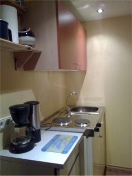A small kitchen with a sink, a refrigerator, and a coffee machine. The walls are painted in a light color and the shelves are well organized.