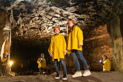 Zwei Kinder in gelben Regenjacken stehen in einer Höhle. Im Hintergrund sind weitere Personen mit Taschenlampen zu sehen.