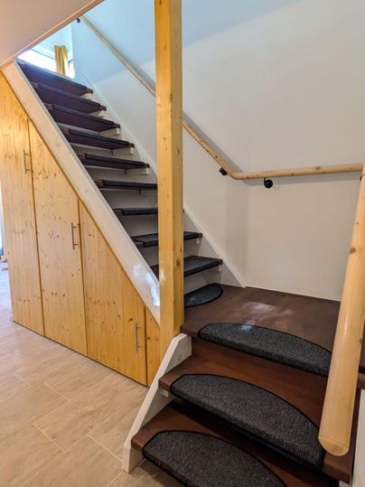 Eine moderne Treppe mit Holzgeländer und Teppichstufen. Neben der Treppe befinden sich Schränke aus Holz.