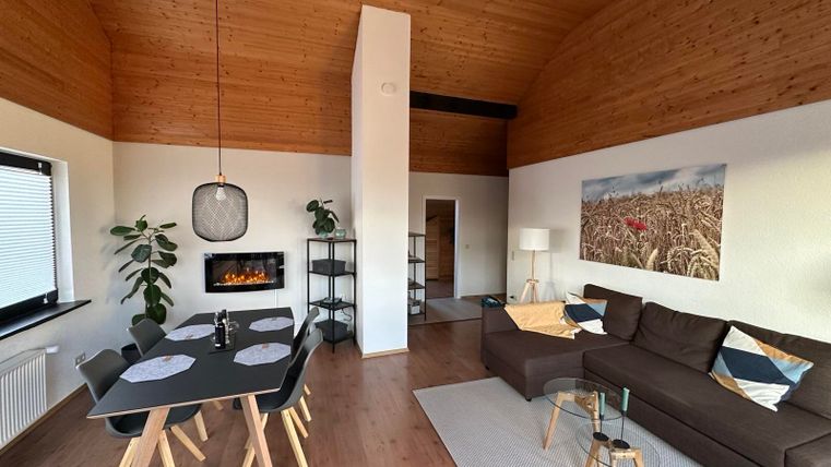 Ein modernes Wohnzimmer mit einem gemütlichen Sofa und einem Esstisch. Die Holzdecke verleiht dem Raum eine warme Atmosphäre.