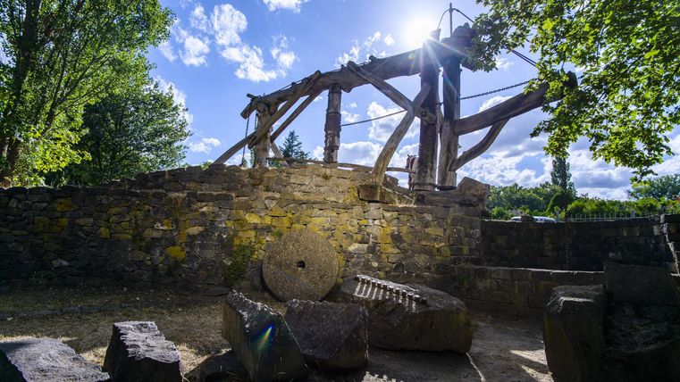 Eine alte Mühle mit Holzstruktur steht in einer grünen Umgebung. Die Sonne scheint durch die Wolken und wirft einen schönen Lichtschein darauf.