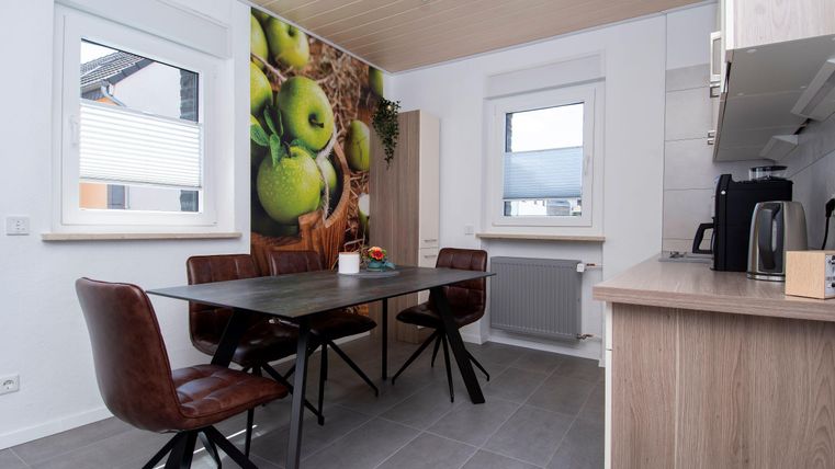 Eine moderne Küche mit einem Tisch und mehreren Stühlen. An der Wand ist ein fruchtiges Motiv mit grünen Äpfeln zu sehen.