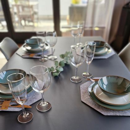 Ein elegant gedeckter Tisch mit Tellern und Gläsern in sanften Farben. Die Tischdekoration umfasst auch eine grüne Pflanze.
