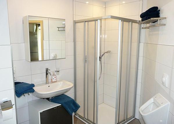 A modern bathroom with a shower, sink, and mirror. The walls are brightly tiled, and blue towels are ready.