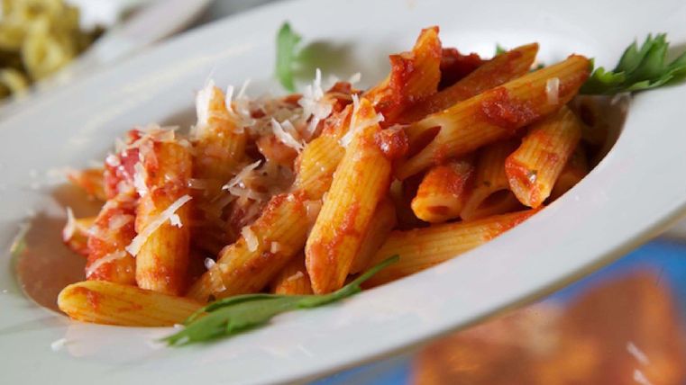 Eine Portion Penne-Nudeln mit Tomatensauce und Parmesan. Das Gericht ist auf einem weißen Teller angerichtet und mit frischen Kräutern garniert.