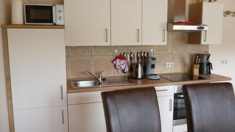 A modern kitchen with white cabinets and a wooden table. On the countertop, kitchen utensils, a kettle, and a coffee machine can be seen.
