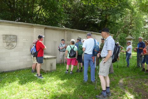 Eine Gruppe von Menschen wandert durch ein Weizenfeld. Im Hintergrund sind sanfte Hügel und Bäume zu sehen.