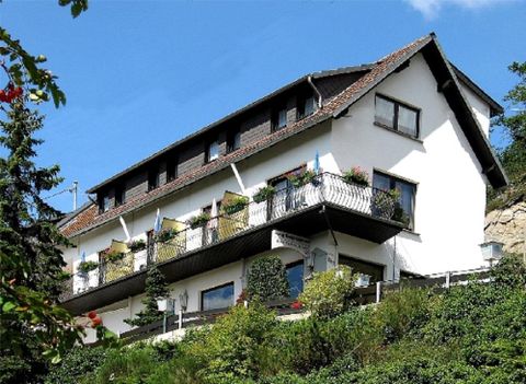 Ein modernes Haus mit mehreren Balkonen, umgeben von Bäumen und Sträuchern. Der Himmel ist klar und blau.