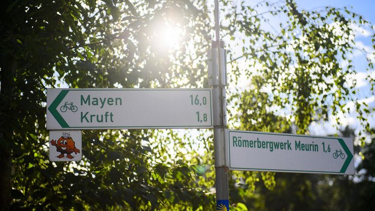 A signpost indicates the distances to Mayen and Krut. The sun is shining and the surroundings are green.