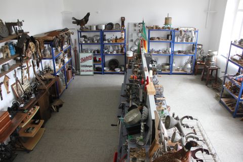 A room full of antique objects and collectibles on shelves. The walls are light, and numerous utensils are carefully arranged.