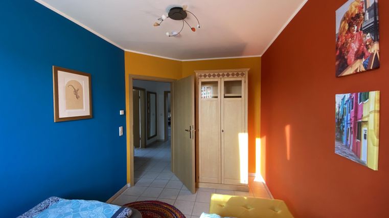 Ein gemütliches Zimmer mit bunten Wänden in Blau und Orange. Zwei Betten stehen neben einem Kleiderschrank.