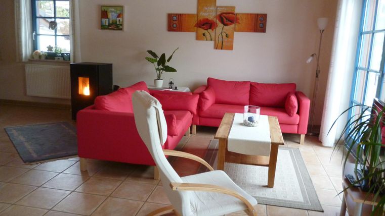 A bright living room with a red sofa and a wooden coffee table. Pictures are hanging on the wall, and a plant stands in the corner.