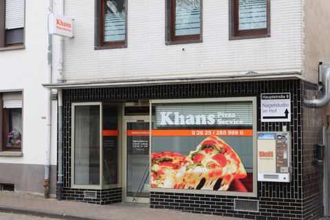 A pizza shop with the sign "Khans Pizza Service". The windows showcase delicious pizzas and information about the offerings.