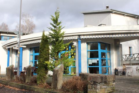 Ein modernes Gebäude mit blauen Fenstern und einer runden Architektur. Im Vordergrund stehen einige Steine und eine kleine Pflanze.