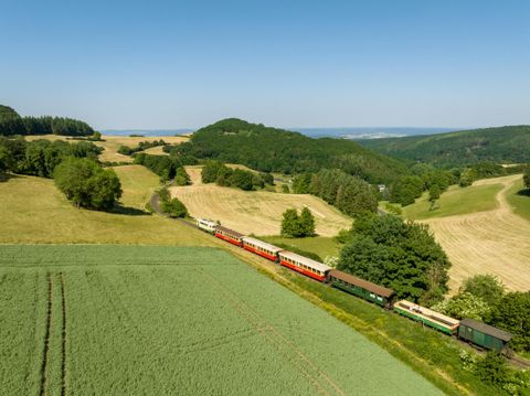 A colorful steam locomotive travels through a green landscape. In the background, there are gentle hills and a blue sky.