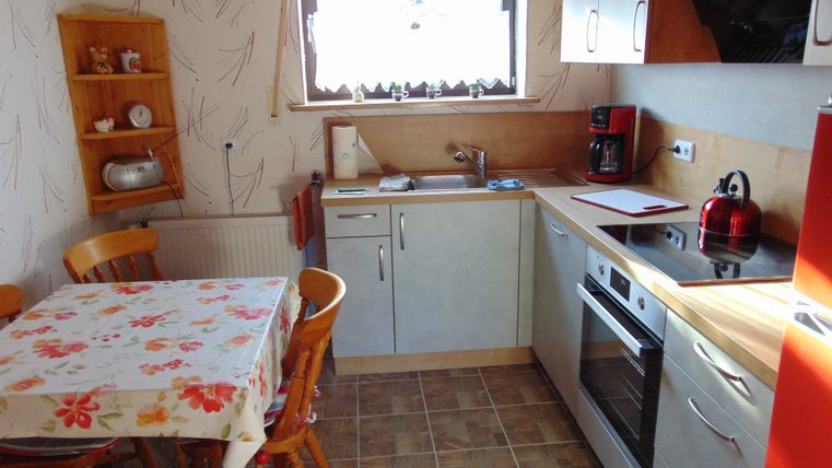 A small, modern kitchen with wooden chairs and a dining table. The kitchen cabinets are light, and a window lets in plenty of daylight.