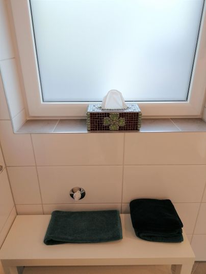 A bathroom with a window and a washbasin. On the table are two towels and a tissue box.