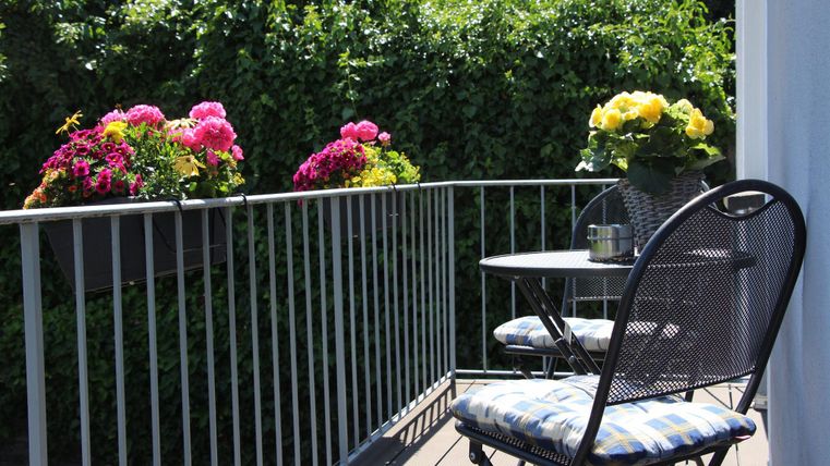 Ein gemütlicher Balkon mit Pflanzen und bunten Blumen. Ein Tisch und ein Stuhl laden zum Entspannen ein.