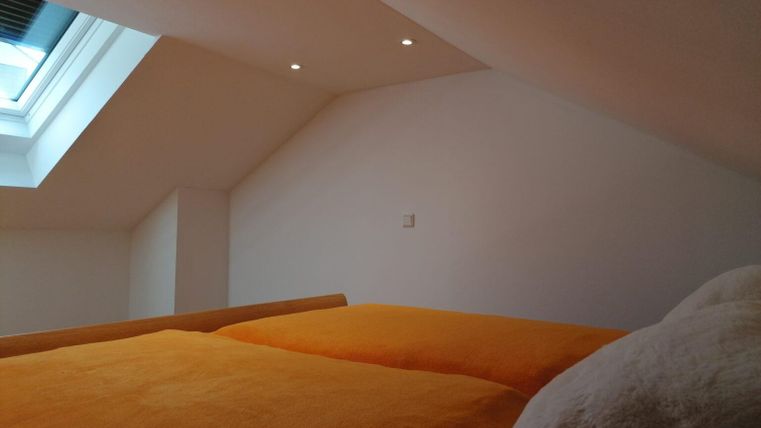 A bright bedroom with a skylight and orange bed covers. The walls are plain and white, creating a friendly atmosphere.