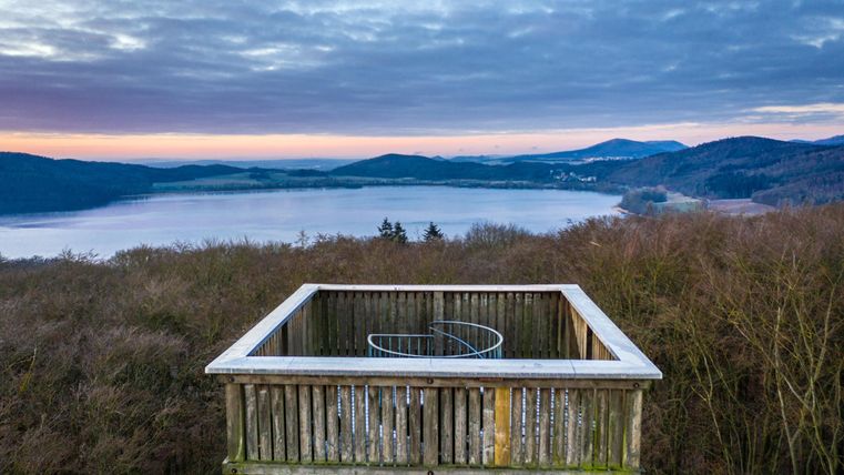 A viewpoint overlooking a lake and surrounding hills. The sky is overcast and the sunrise provides a soft illumination.
