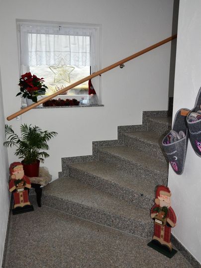 Ein Treppenhaus mit grauen Stufen und einem Handlauf. Auf der Treppe stehen zwei dekorative Figuren und eine Pflanze in einem Topf.