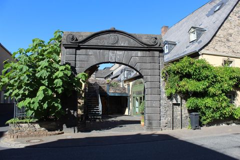 Ein historisches Tor mit einer eleganten Steinarchitektur. Darum herum sind grüne Bäume und charmante Gebäude.