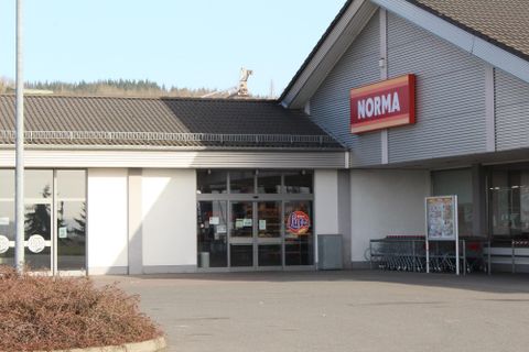 Ein Norma-Supermarkt mit großen Fenstern und einem roten Schild. Vor dem Gebäude stehen Einkaufswagen bereit.