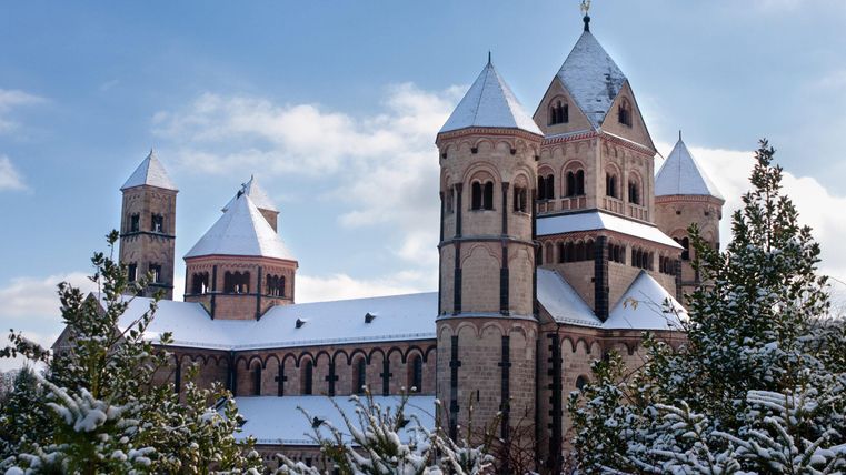 Eine beeindruckende Kirche mit Türmen und schneebedecktem Dach. Umgeben von Tannenbäumen im Winter.