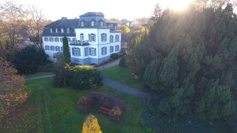 Ein elegantes Gebäude umgeben von einem gepflegten Garten. Die Sonne scheint im Hintergrund und zaubert eine angenehme Atmosphäre.