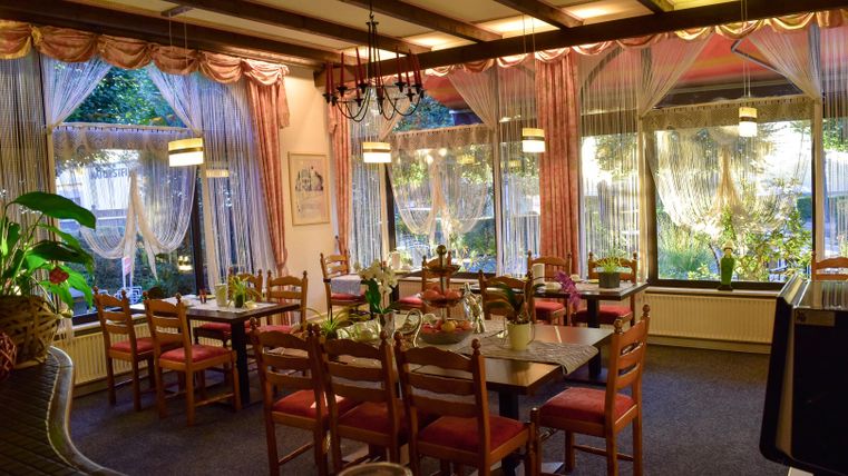 Ein einladendes Restaurant mit Holzmöbeln und einem gemütlichen Ambiente. Große Fenster lassen viel Tageslicht herein und bieten einen Blick ins Grüne.