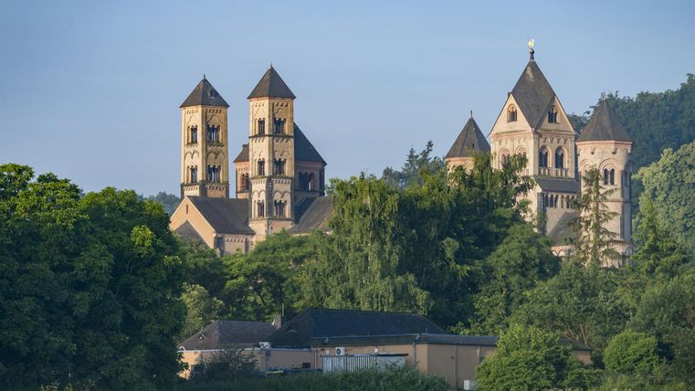 An old architecture with towers amid green trees. The sky is clear and conveys a peaceful atmosphere.