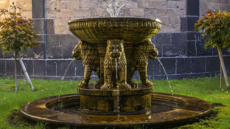Ein schöner Brunnen mit Löwenfiguren. Wasser sprudelt aus dem Brunnen und umgibt grünes Gras.